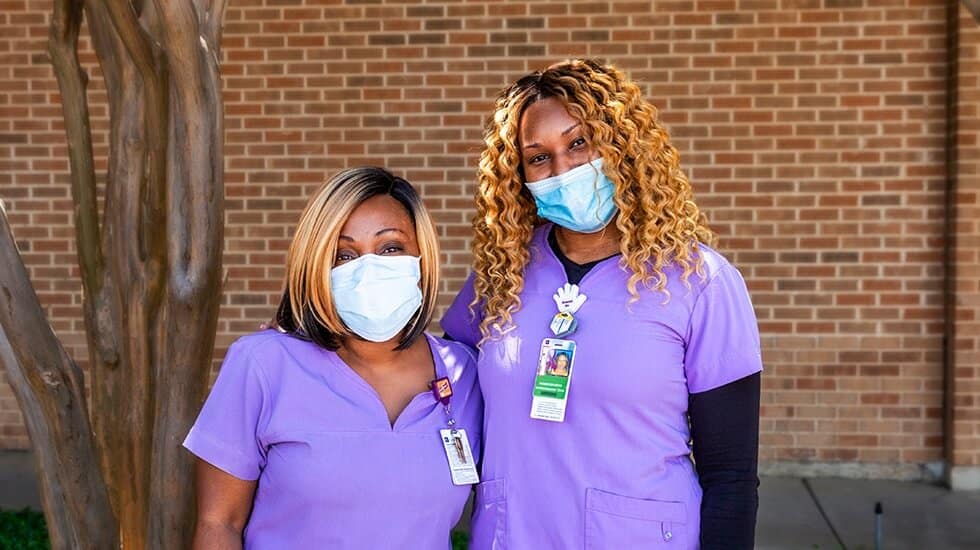 Two female patient navigators in purple scrubs